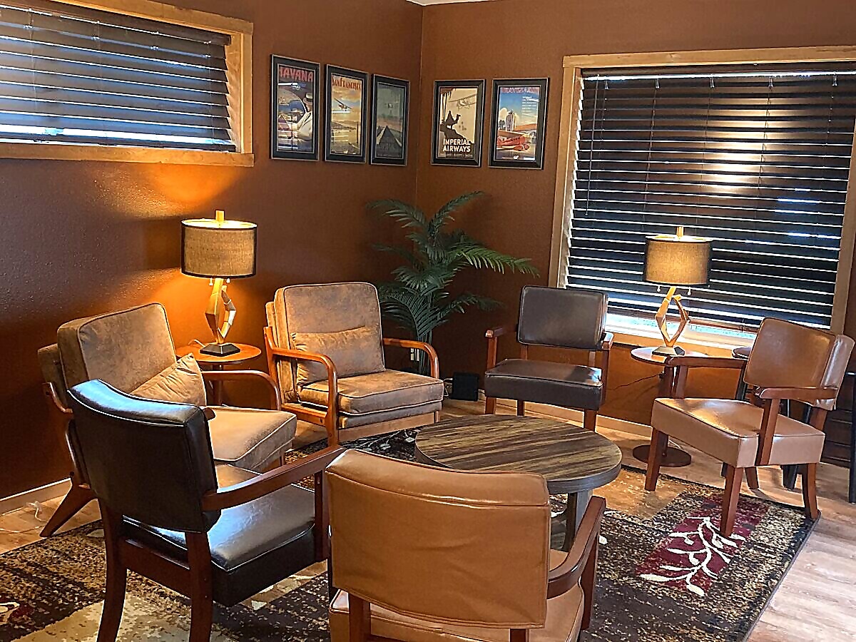 Groom's room aviation-themed lounge with leather chairs and vintage travel posters at Sandy River Airport