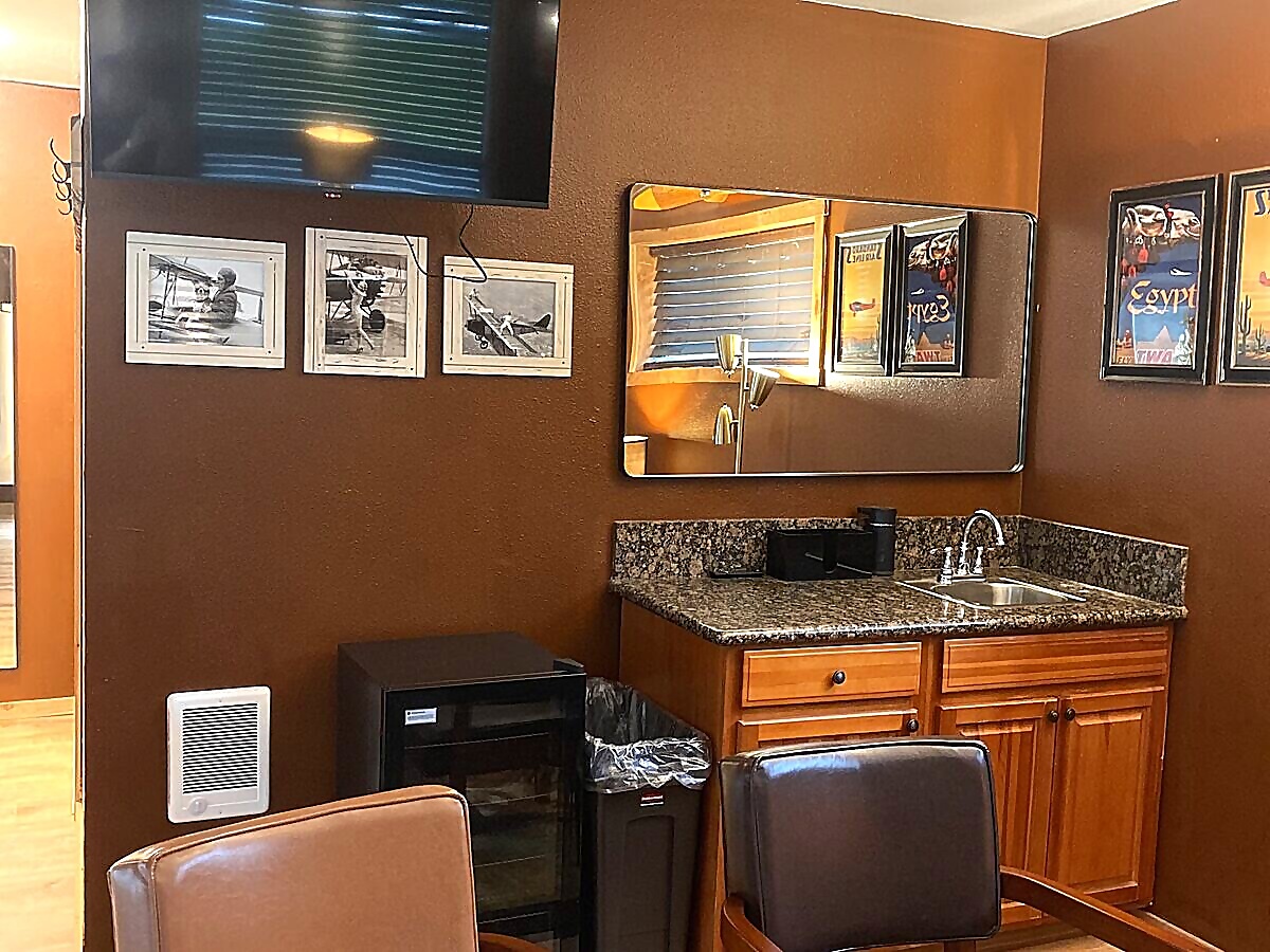 Groom's room with flat-screen TV, biplane prints, and seating area at Sandy River Airport wedding venue