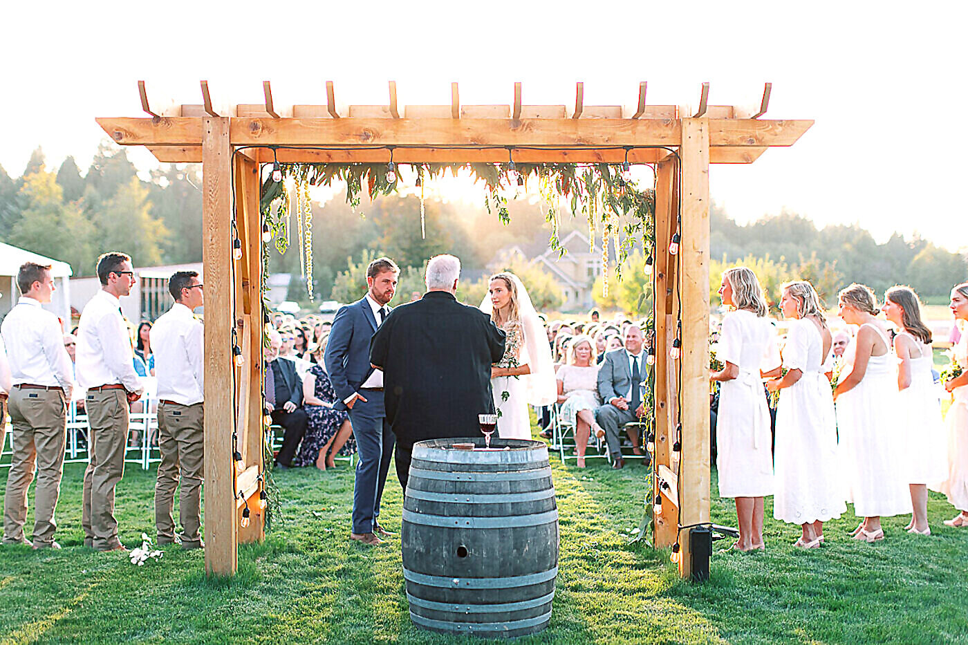 Wedding ceremony under string-light arbor at golden hour at Sandy River Airport outdoor venue in Sandy, Oregon
