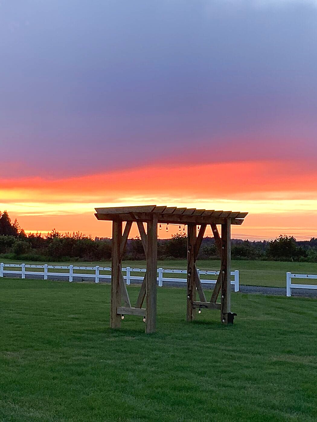 Wooden ceremony arbor at sunset with string lights at Sandy River Airport wedding venue